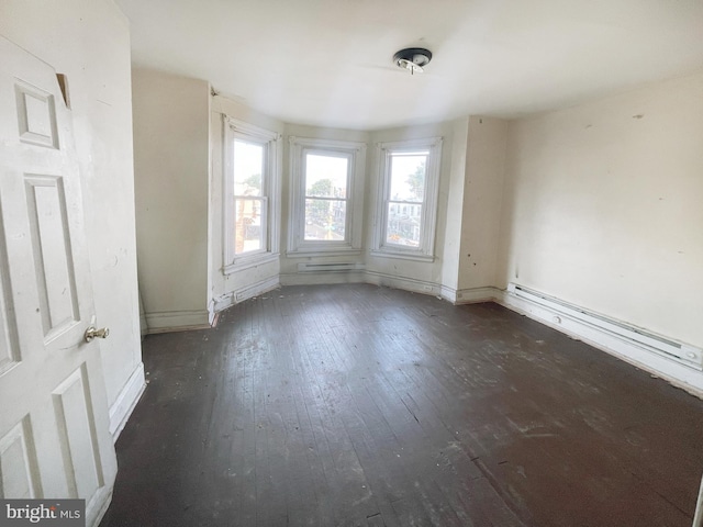 spare room featuring baseboard heating and dark wood-type flooring