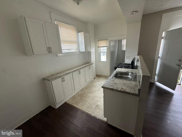 kitchen with black stove, light hardwood / wood-style floors, white cabinetry, and sink