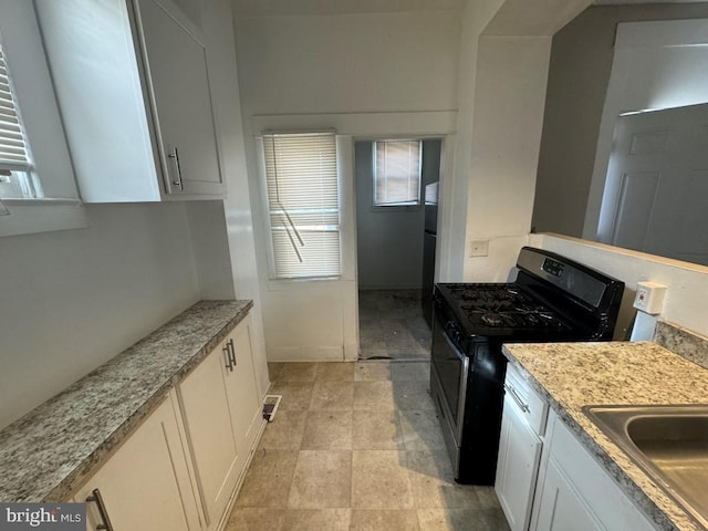 kitchen with white cabinets, light stone countertops, and stainless steel gas range