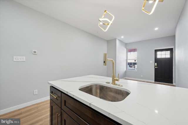 kitchen with sink, light hardwood / wood-style flooring, decorative light fixtures, light stone counters, and dark brown cabinets