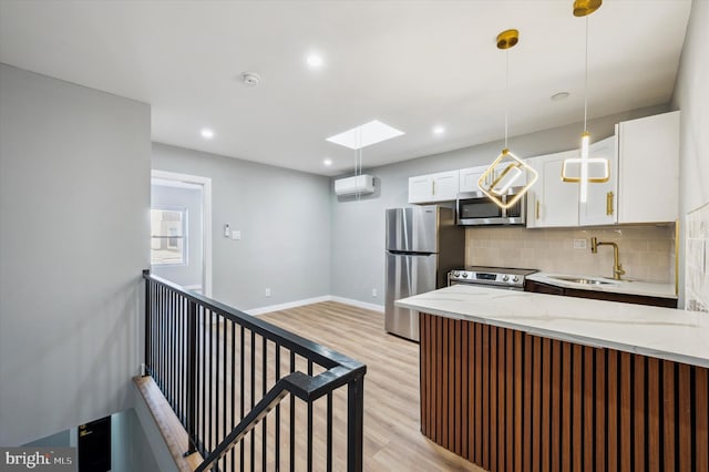 kitchen with appliances with stainless steel finishes, a skylight, sink, white cabinets, and light hardwood / wood-style floors