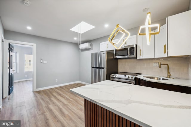 kitchen featuring a skylight, sink, hanging light fixtures, stainless steel appliances, and white cabinets