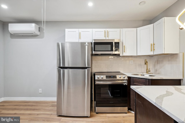 kitchen featuring a wall mounted air conditioner, sink, light hardwood / wood-style flooring, appliances with stainless steel finishes, and white cabinetry