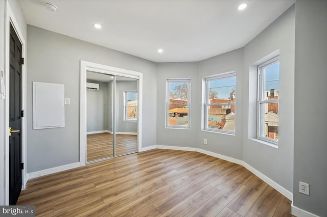 unfurnished bedroom with a wall unit AC, a closet, and light hardwood / wood-style floors