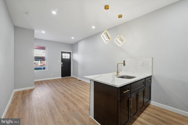 kitchen with kitchen peninsula, light wood-type flooring, light stone counters, sink, and decorative light fixtures