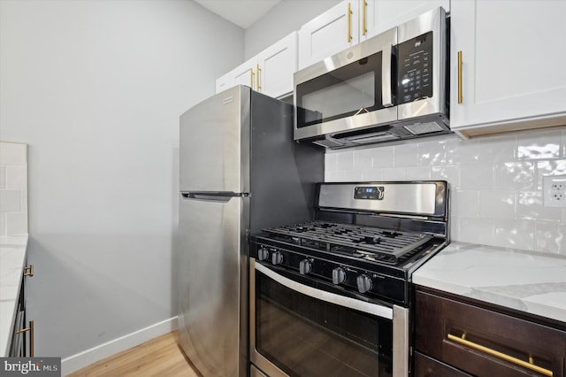 kitchen featuring decorative backsplash, light stone countertops, stainless steel appliances, white cabinets, and light hardwood / wood-style floors