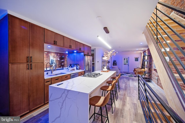 kitchen with sink, a kitchen bar, hardwood / wood-style flooring, a kitchen island, and appliances with stainless steel finishes