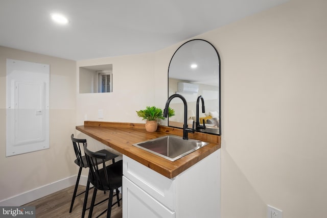 kitchen with a wall mounted air conditioner, sink, wood-type flooring, electric panel, and butcher block counters