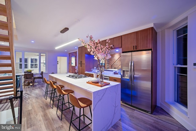 kitchen featuring a breakfast bar, stainless steel appliances, crown molding, pendant lighting, and light hardwood / wood-style flooring