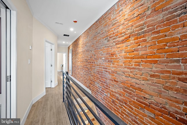 hallway featuring light wood-type flooring, crown molding, and brick wall