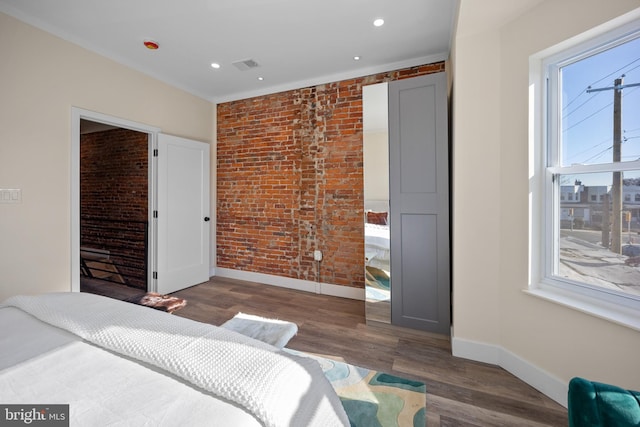 bedroom with dark hardwood / wood-style floors, ornamental molding, and brick wall