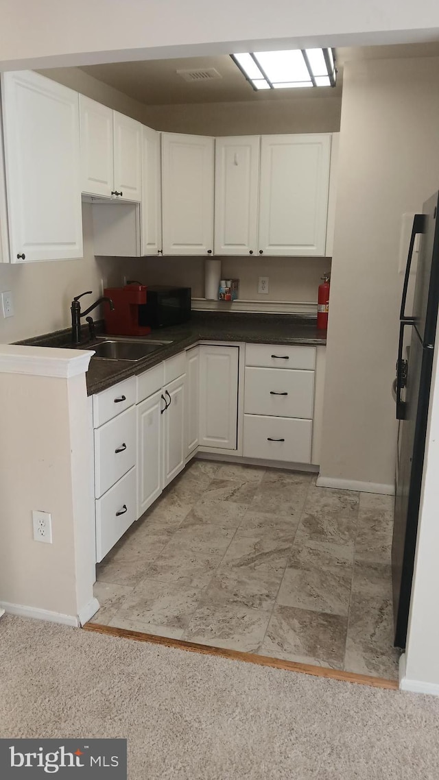 kitchen featuring white cabinets, stainless steel refrigerator, and sink