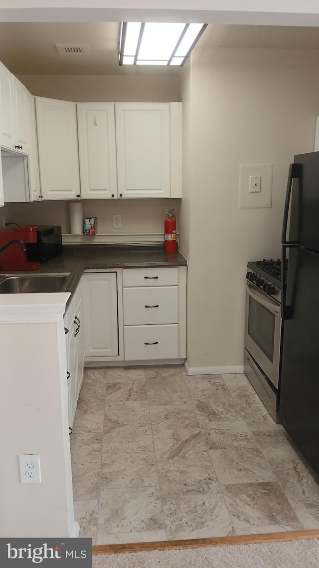 kitchen with sink, white cabinetry, black fridge, and stainless steel range with gas stovetop