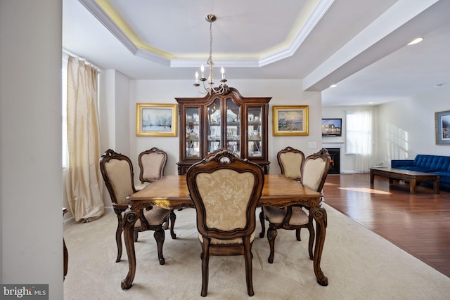 dining area with a raised ceiling, crown molding, light hardwood / wood-style floors, and an inviting chandelier