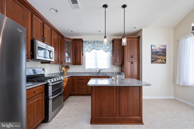 kitchen featuring a center island, sink, hanging light fixtures, appliances with stainless steel finishes, and light stone counters