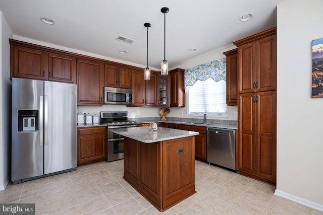 kitchen with a center island, sink, light stone countertops, appliances with stainless steel finishes, and decorative light fixtures