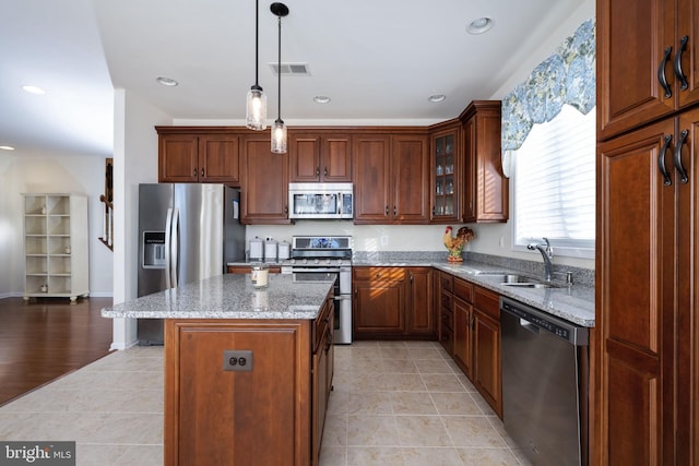 kitchen with sink, hanging light fixtures, stainless steel appliances, light stone counters, and a kitchen island