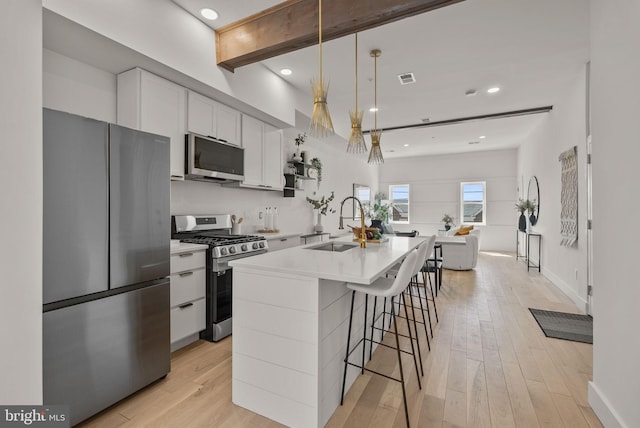 kitchen featuring pendant lighting, light wood-type flooring, an island with sink, appliances with stainless steel finishes, and white cabinetry