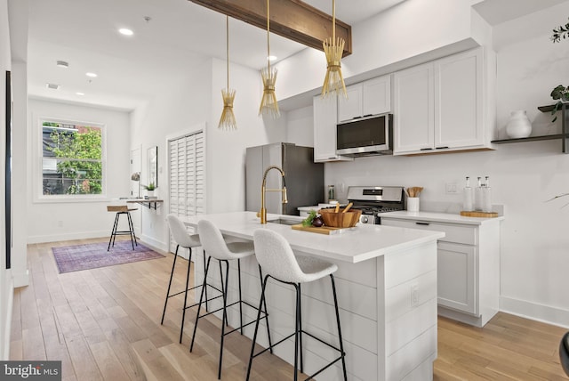 kitchen featuring a center island with sink, stainless steel appliances, decorative light fixtures, and light hardwood / wood-style flooring