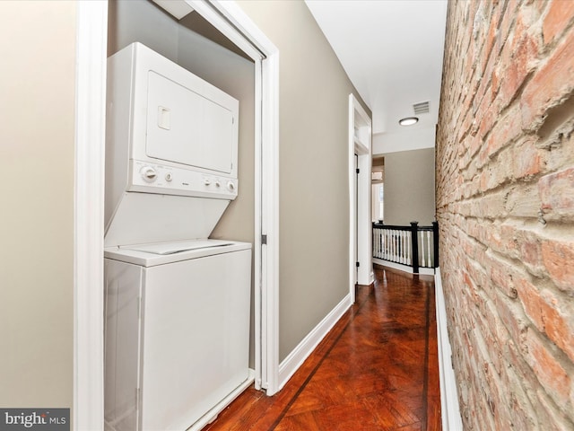 clothes washing area with stacked washer and dryer and dark parquet floors