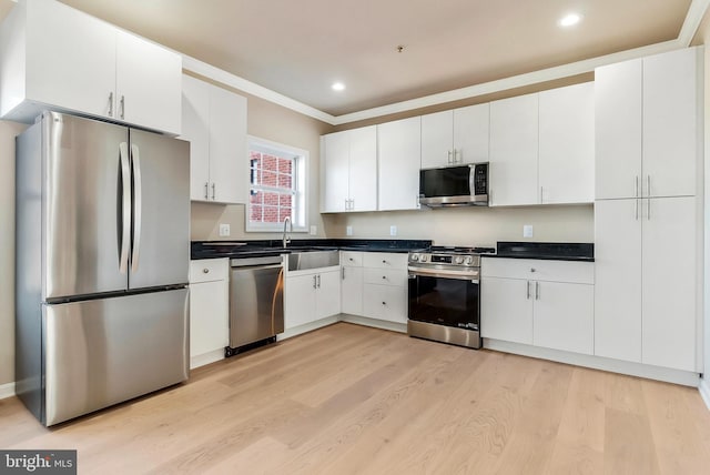 kitchen with appliances with stainless steel finishes, light wood-type flooring, ornamental molding, sink, and white cabinets