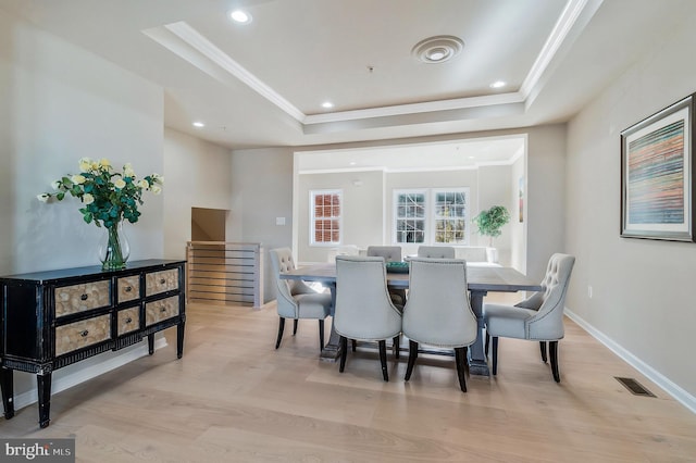 dining room with light hardwood / wood-style floors, crown molding, and a tray ceiling