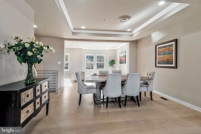 dining room featuring a raised ceiling, light wood-type flooring, and ornamental molding