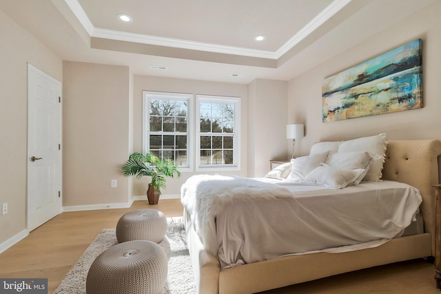 bedroom with light hardwood / wood-style floors, a raised ceiling, and ornamental molding