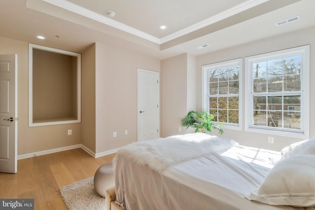 bedroom with light hardwood / wood-style floors, a raised ceiling, and crown molding