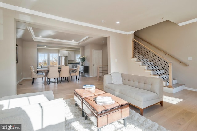 living room with a raised ceiling, ornamental molding, and light hardwood / wood-style flooring