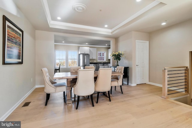 dining area with a tray ceiling, ornamental molding, and light wood-type flooring