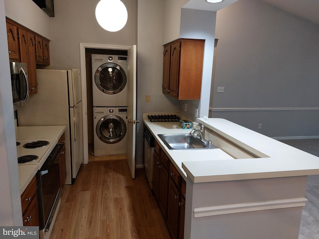 kitchen featuring stacked washer and dryer, sink, light wood-type flooring, and electric stove