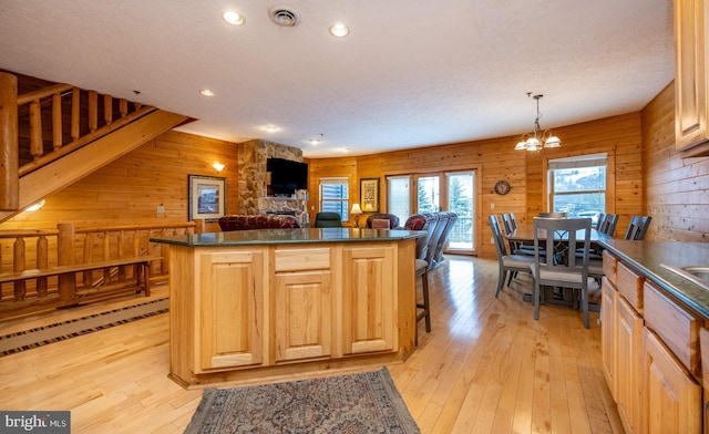 kitchen featuring pendant lighting, an inviting chandelier, wooden walls, light wood-type flooring, and a kitchen island