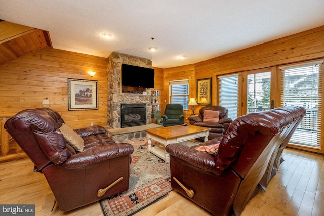 living room with wood walls, a fireplace, vaulted ceiling, and light wood-type flooring