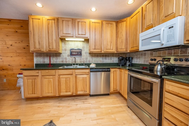 kitchen with sink, tasteful backsplash, light hardwood / wood-style flooring, wood walls, and appliances with stainless steel finishes