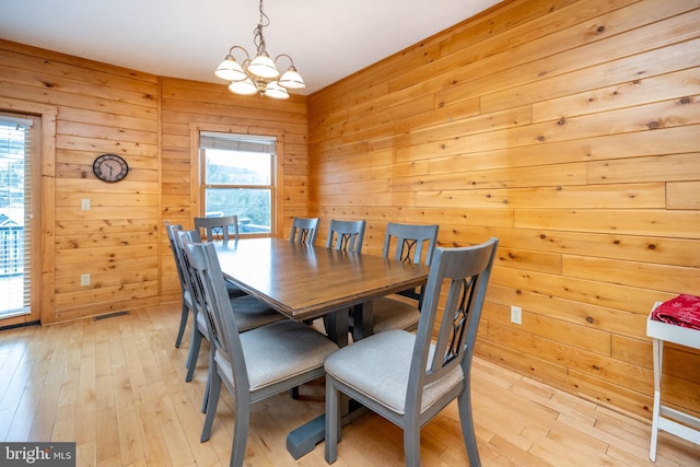 dining room featuring an inviting chandelier, wooden walls, and light hardwood / wood-style flooring