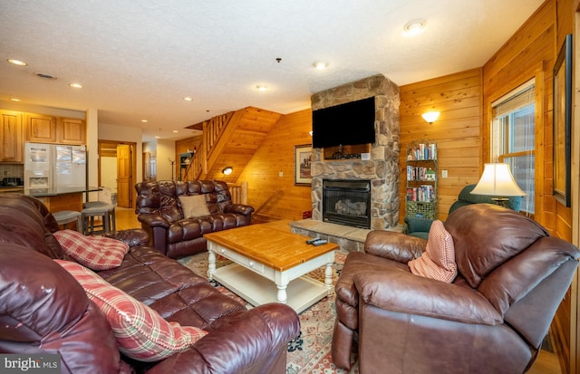 living room with a textured ceiling, a stone fireplace, and wood walls