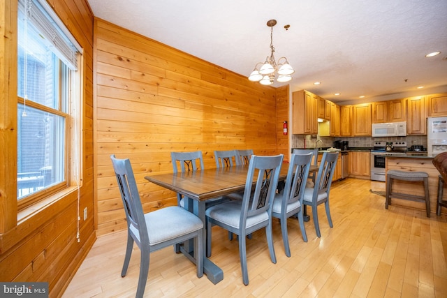 dining area featuring wooden walls, light hardwood / wood-style flooring, sink, and a notable chandelier