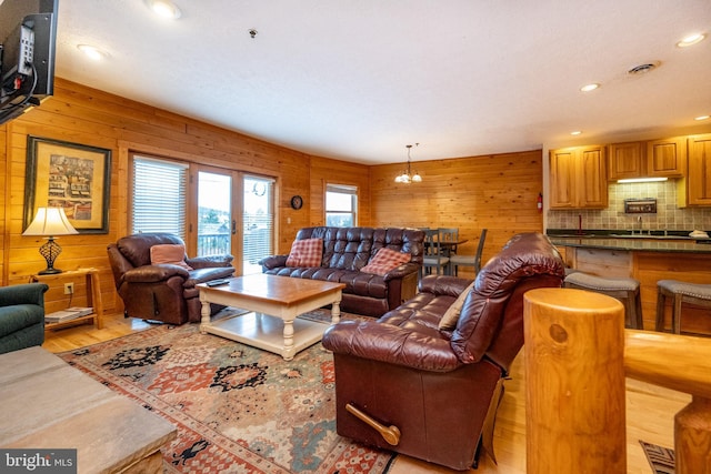 living room featuring light hardwood / wood-style floors, an inviting chandelier, and wooden walls