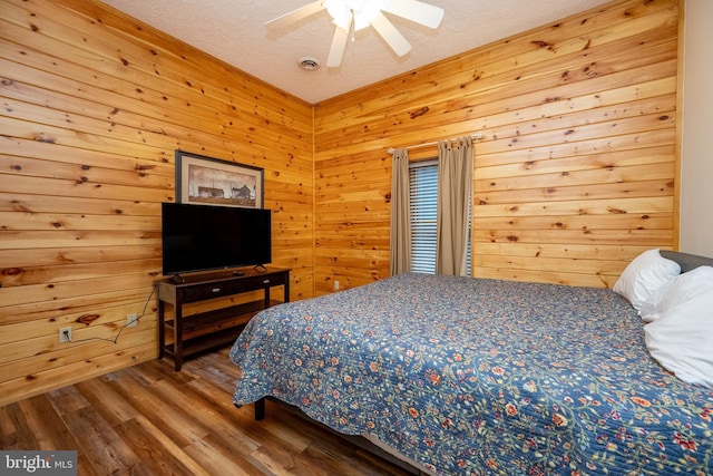 bedroom featuring wood-type flooring, a textured ceiling, ceiling fan, and wooden walls