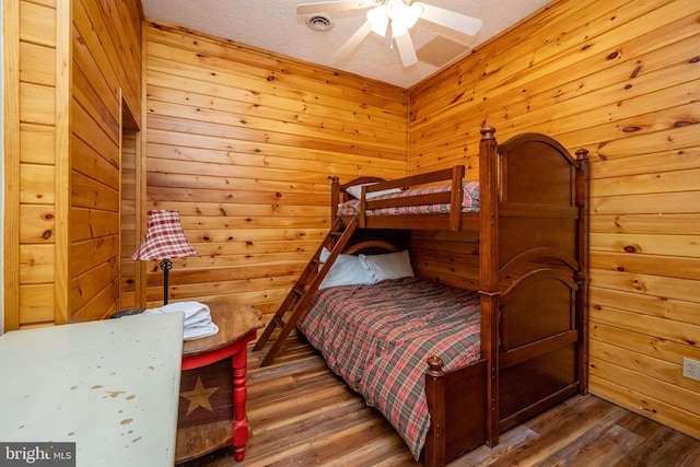 bedroom featuring a textured ceiling, hardwood / wood-style flooring, ceiling fan, and wood walls