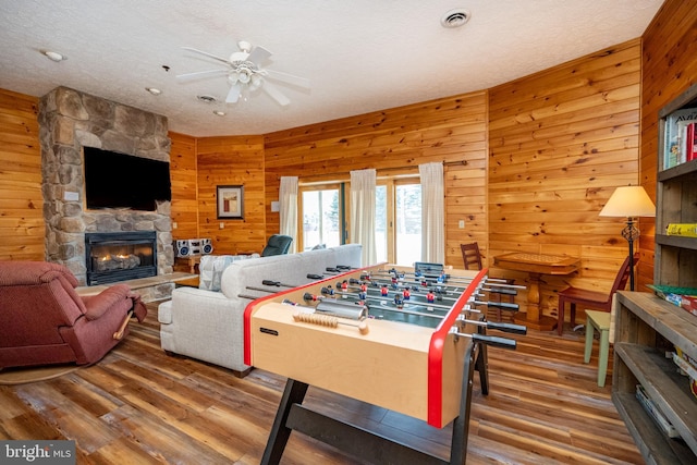 playroom with ceiling fan, a fireplace, wood-type flooring, and wooden walls