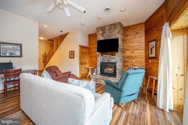 living room with wood walls, a stone fireplace, ceiling fan, a textured ceiling, and wood-type flooring