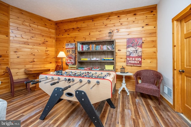 recreation room with hardwood / wood-style floors, wood walls, and a textured ceiling