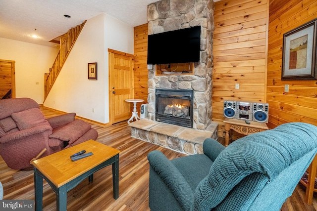 living room featuring a textured ceiling, hardwood / wood-style flooring, a stone fireplace, and wooden walls