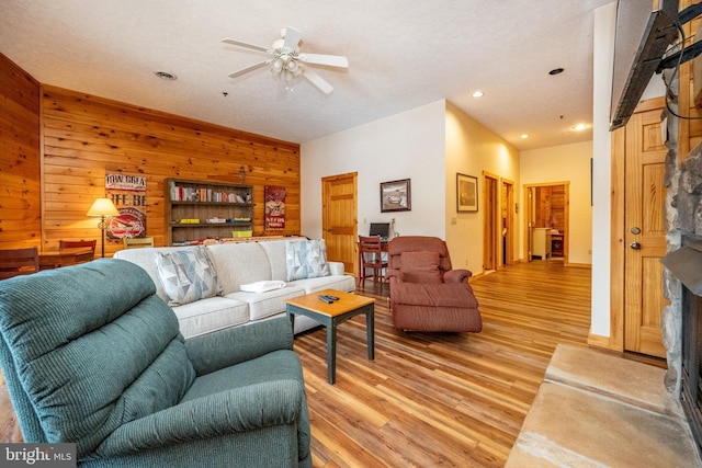 living room with ceiling fan, wood-type flooring, a textured ceiling, and wooden walls