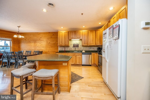 kitchen with hanging light fixtures, stainless steel appliances, wood walls, a chandelier, and a kitchen bar