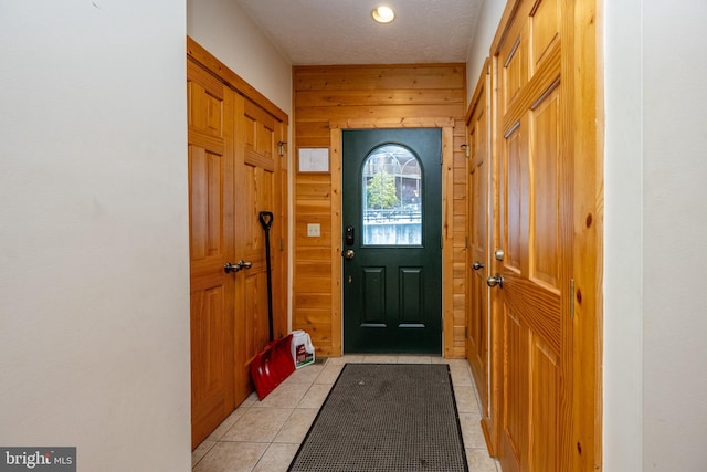 doorway with light tile patterned floors, a textured ceiling, and wooden walls