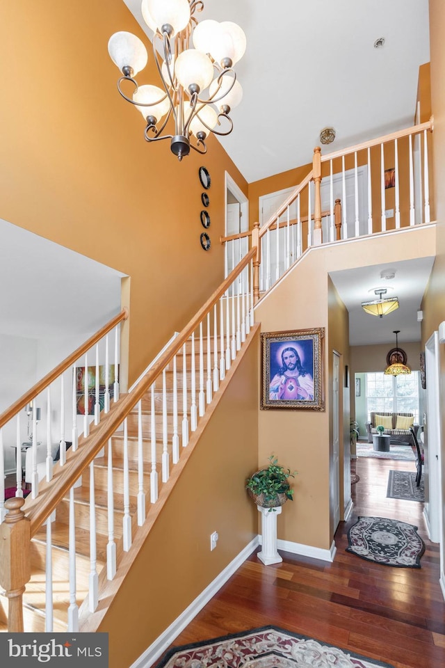 stairs with a high ceiling, hardwood / wood-style flooring, and an inviting chandelier