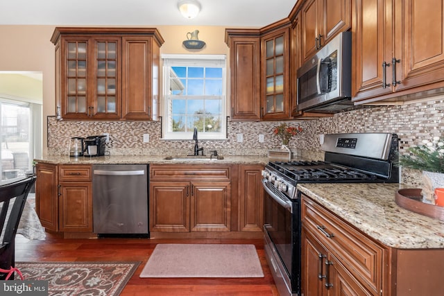 kitchen with sink, dark wood-type flooring, stainless steel appliances, light stone counters, and backsplash